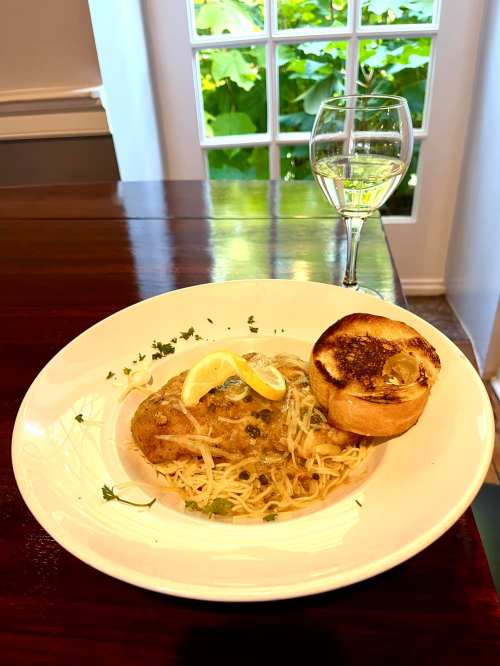 A plate of pasta with a lemon slice and a piece of toasted bread, accompanied by a glass of white wine.