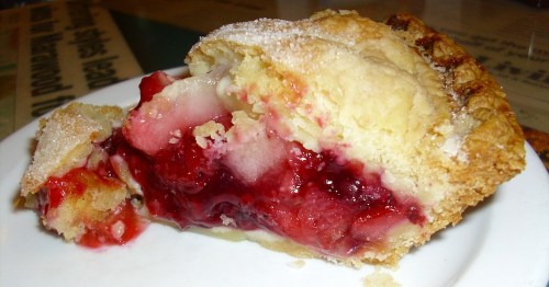 A slice of cherry pie on a white plate, showcasing a flaky crust and vibrant red filling.