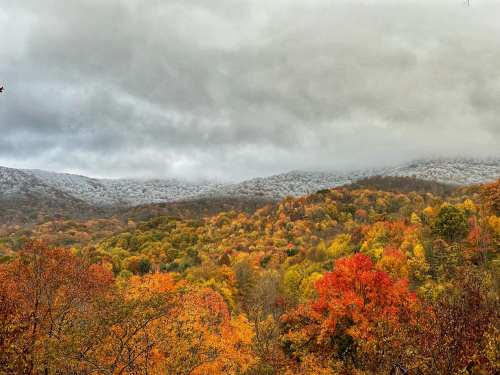 A scenic view of mountains covered in autumn foliage, with vibrant orange and yellow trees under a cloudy sky.