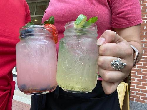 Two mason jars filled with colorful drinks, one pink with berries and one green with lime, held by a person.