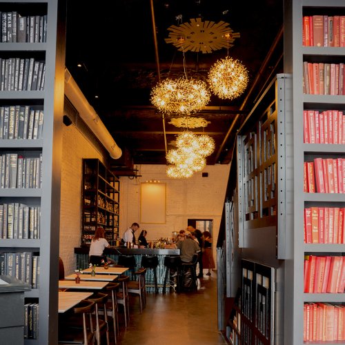 A modern restaurant interior with bookshelves, stylish lighting, and diners enjoying their meals.