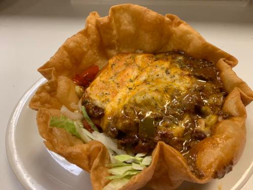 A crispy tortilla bowl filled with lettuce, tomatoes, onions, and a cheesy meat mixture.
