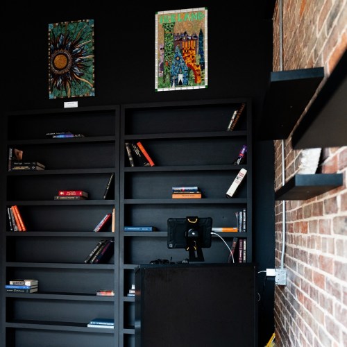 A dark room with empty bookshelves, colorful artwork on the wall, and a small black device on a table.