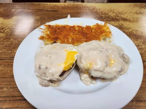 A plate with two biscuits topped with sausage gravy and eggs, alongside crispy hash browns.