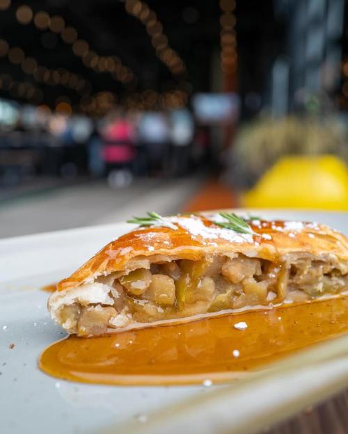 A close-up of a golden pastry filled with a savory mixture, drizzled with sauce, on a plate with a blurred background.