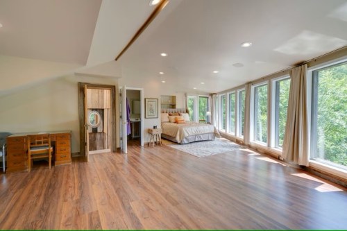 Spacious, well-lit bedroom with large windows, wooden floors, and a cozy bed, featuring a desk and a mirror.
