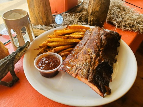 A plate with BBQ ribs, golden fries, and a small cup of sauce, set on a rustic table with decorative elements.