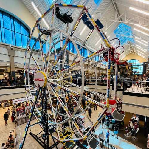 A colorful indoor Ferris wheel at Scheels, surrounded by shoppers in a spacious retail environment.