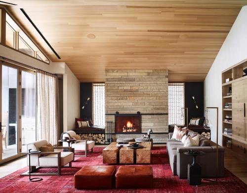 Cozy living room with a stone fireplace, wooden ceiling, modern furniture, and a vibrant red rug.