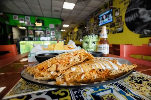 A plate of quesadillas with sauce, chips, and a beer in a colorful restaurant setting.