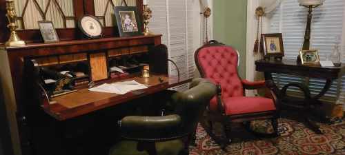 A vintage office with a wooden desk, a pink armchair, and framed photos on the walls, creating a cozy atmosphere.