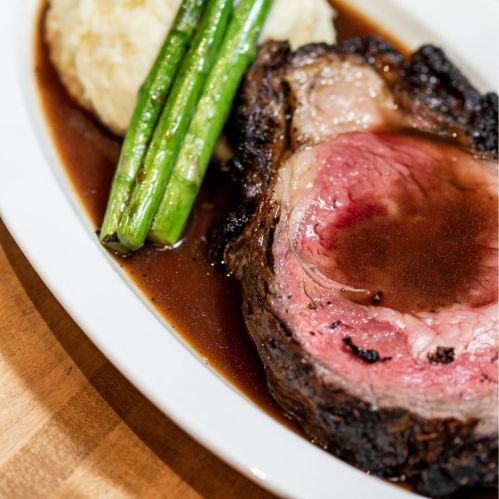 A plate featuring a juicy slice of roast beef, creamy mashed potatoes, and green asparagus drizzled with sauce.