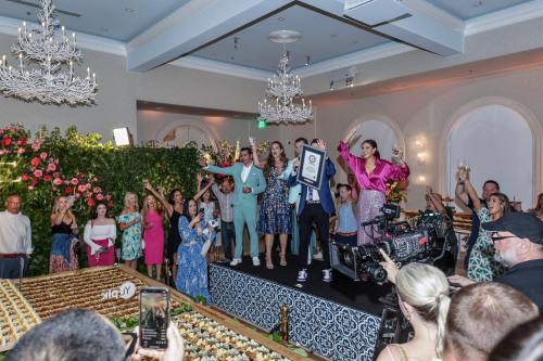 A celebratory event with people cheering, holding a certificate, and a large display of food in a decorated venue.