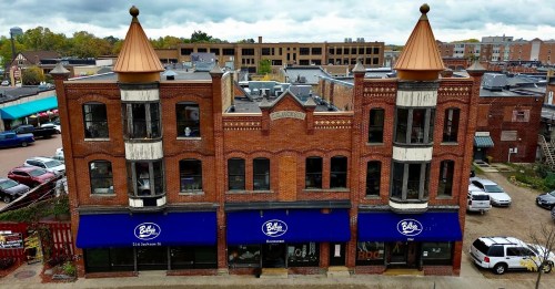 Historic brick buildings with copper-topped towers, featuring blue awnings and a bustling urban backdrop.