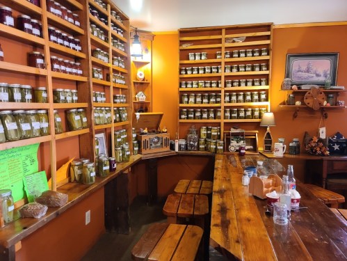 A cozy shop interior with wooden shelves filled with jars of spices and preserves, and a rustic wooden table.