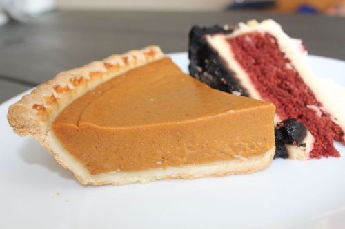 A slice of pumpkin pie next to a slice of red velvet cake on a white plate.