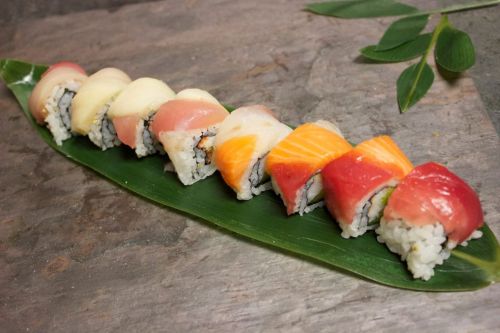 A variety of sushi rolls arranged on a green leaf, showcasing colorful fish and rice fillings.