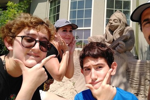 A group of four people posing playfully in front of a sand sculpture of a woman playing a guitar.