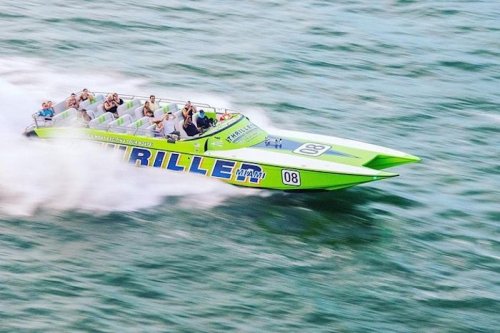 A bright green speedboat with passengers speeds across the water, creating a spray as it moves swiftly.