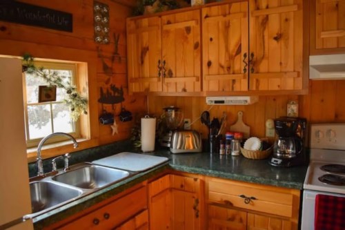 Cozy wooden kitchen with a green countertop, sink, coffee maker, and various kitchen utensils and decor.