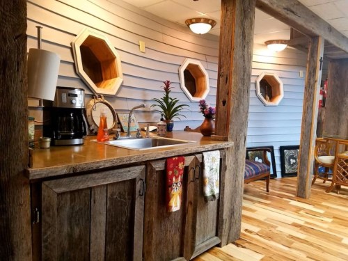 A rustic kitchen with a wooden counter, coffee maker, and decorative mirrors on the wall, featuring wooden flooring.