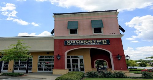 Exterior of a restaurant building with a sign reading "Squish Inn Pizza Factory," under a blue sky with clouds.
