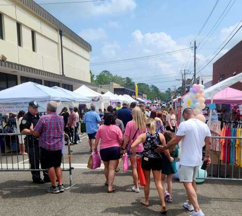 A bustling street fair with colorful tents, people walking, and a clear blue sky in the background.