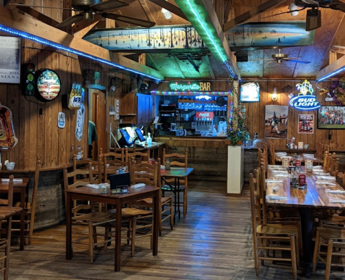 Cozy restaurant interior with wooden decor, tables, and a bar area illuminated by blue lights.