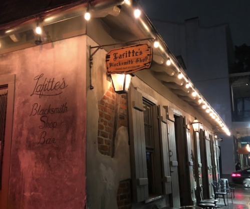 A dimly lit exterior of Lafitte's Blacksmith Shop Bar, featuring a sign and warm string lights at night.