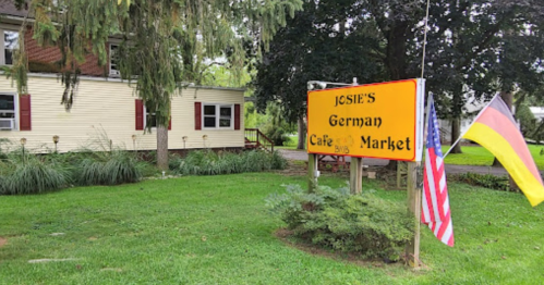 Sign for "Josie's German Cafe & Market" with an American flag and a German flag in a grassy area.