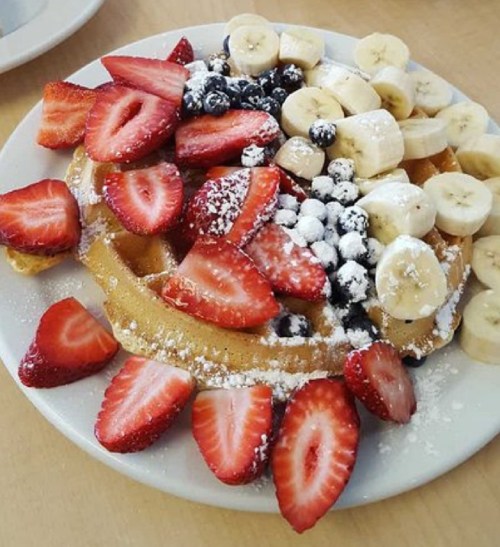 A plate of waffles topped with sliced strawberries, bananas, blueberries, and powdered sugar.