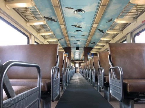 Interior of a train with brown seats and a ceiling painted like a blue sky with birds flying.
