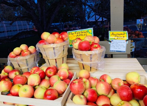 Baskets of red and yellow apples on a wooden table, with signs for "Field Grown Apples" and "Autumn Crisp."