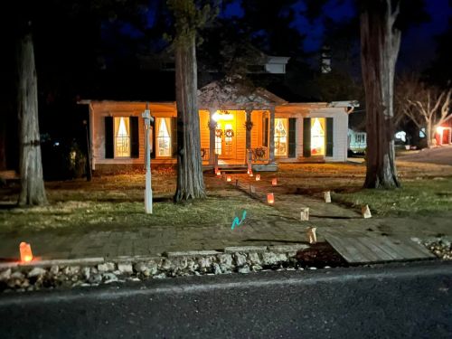 A warmly lit house at night, with glowing lanterns lining the path and trees framing the scene.