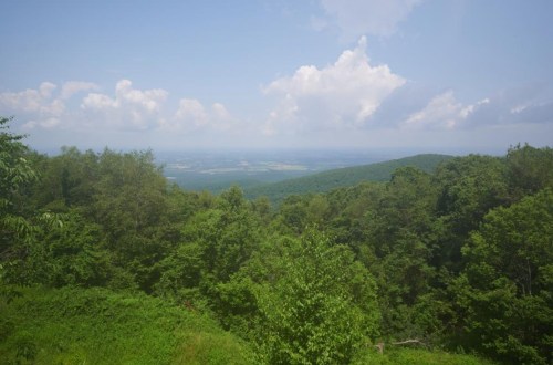 A scenic view of lush green mountains under a blue sky with fluffy white clouds.