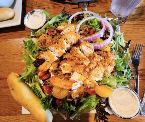 A large salad topped with grilled chicken, red onions, and mixed greens, served with a breadstick and dressing on the side.