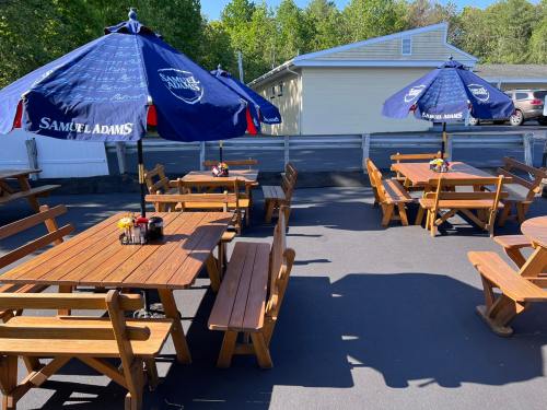 Outdoor seating area with wooden tables and blue umbrellas, featuring a Samuel Adams logo, surrounded by greenery.