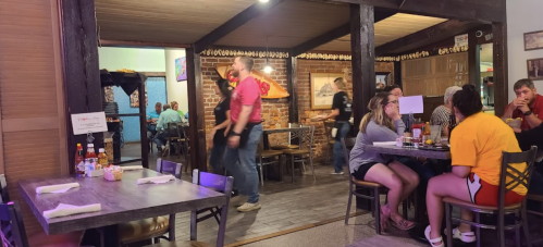 A cozy restaurant scene with diners at tables, a brick wall, and staff serving food in a warm, inviting atmosphere.