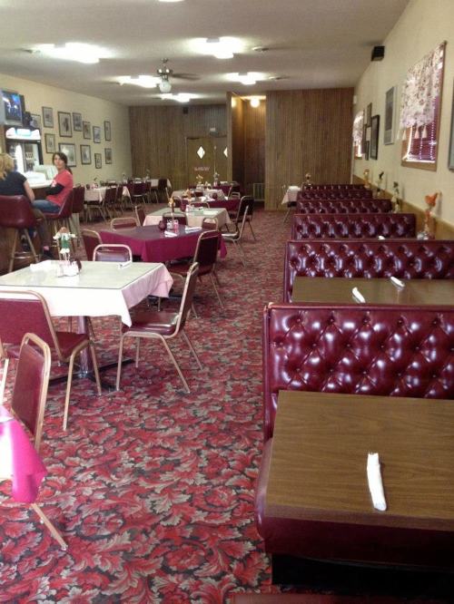 A cozy restaurant interior with red booths, tables, and floral carpet, featuring framed pictures on the walls.