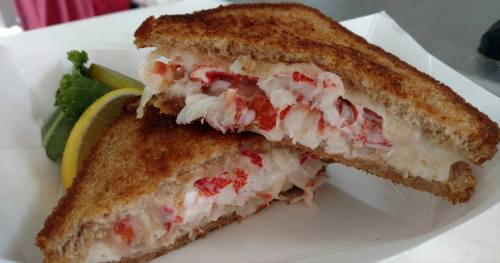 A toasted lobster sandwich with chunks of lobster meat, served with a lemon wedge and a piece of lettuce.