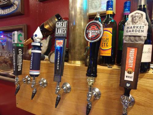 A row of beer taps featuring various craft beers and breweries, with colorful labels and handles.