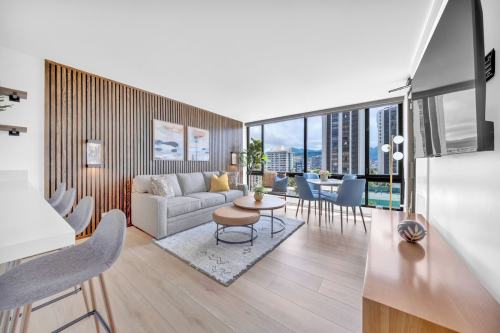 Modern living room with a gray sofa, wooden accents, and large windows overlooking a cityscape. Bright and airy atmosphere.