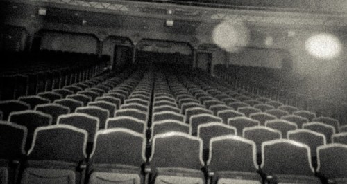 A dimly lit theater with rows of empty seats stretching into the distance.