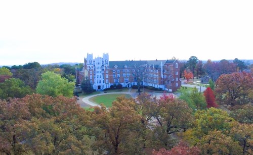 Aerial view of a large brick building surrounded by colorful autumn trees and a grassy area.