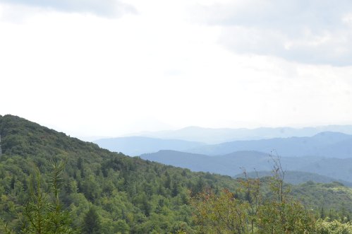 A scenic view of rolling green hills and distant mountains under a cloudy sky.