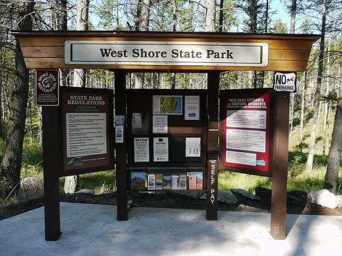 Signage at West Shore State Park displaying regulations, maps, and information in a forested area.