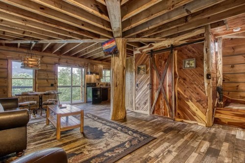 Cozy cabin interior with wooden beams, a rustic table, and large windows showcasing a natural view.