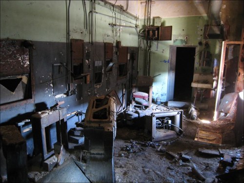 An abandoned, dimly lit room with old machinery, peeling paint, and debris scattered on the floor.