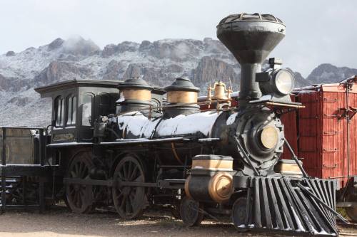 A vintage steam locomotive covered in snow, set against a backdrop of mountains.