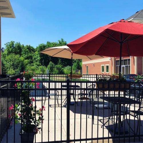 A sunny outdoor patio with tables, umbrellas, and greenery in the background.